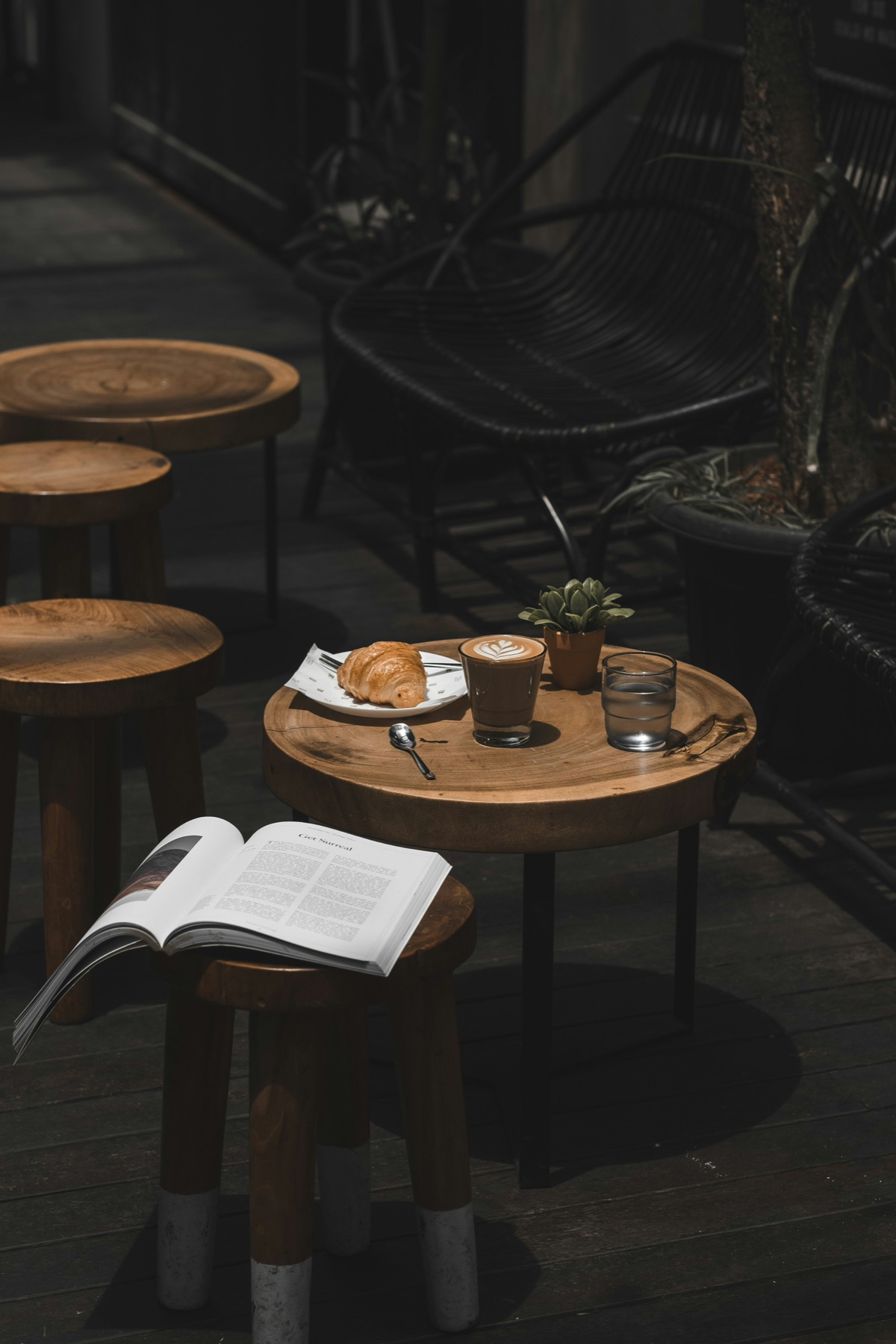 A croissant, a coffee and an open book on a round wooden table