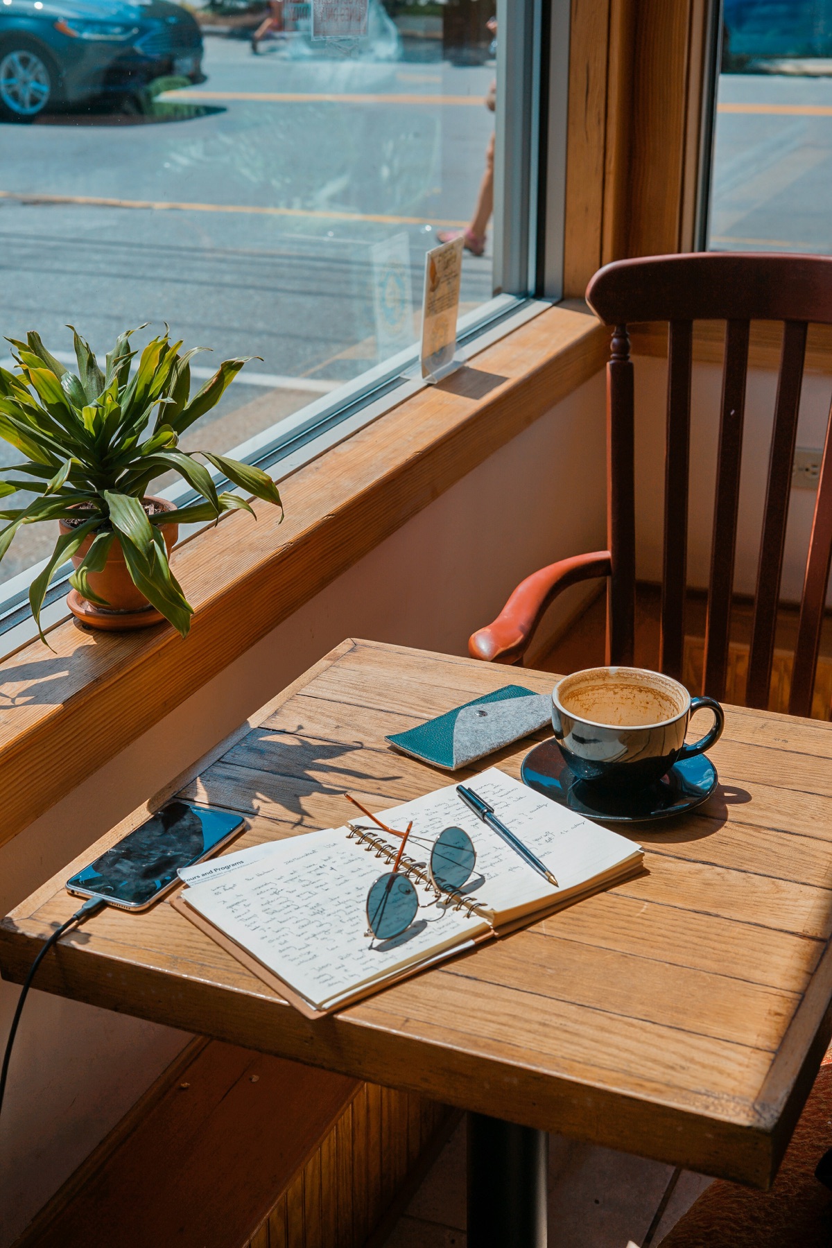 A window table with a coffee, a notebook and a plant